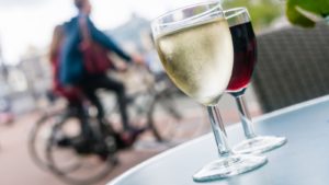 Zwei Weingläser stehen auf einem Tisch und zwei Fahrradfahrer sind verschwommen im Hintergrund