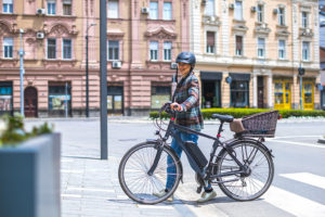 Eine Frau schiebt glücklich ihr gebrauchtes E-Bike über die Straße.